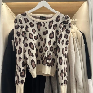 Leopardmönstrad stickad tröja Chica London - Snygg stickad tröja från Chica London i beige med brunt leopardmönster. Modellen är croppad med puffiga axlar och rund halsringning. Perfekt för dig som vill sticka ut med ett trendigt djurmönster och cool passform.