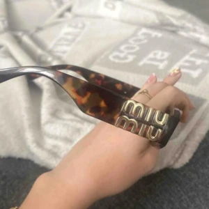 Miu Miu bruna kattögda solglasögon - Snygga kattögda solglasögon från Miu Miu med brunmelerat sköldpaddsmönster och stora guldiga loggor på skalmarna. Glasögonen har en cool, retroinspirerad form och är tillverkade i plast. Perfekta för dig som vill sticka ut med en lyxig vibe.