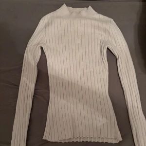 Vit ribbad polotröja från Bik Bok - Säljer en ribbad polotröja från Bik Bok i storlek XS. Tröjan har lång ärm, hög hals och är figurnära med stretchigt material. Perfekt att styla med jeans eller kjol för en clean look. Knappt använd. Den har en liten rosa ton