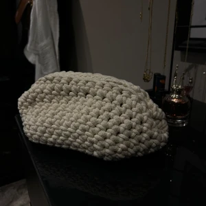 Clutch väska - Säljer en chunky, handstickad clutch i beige färg. Väskan har en mjuk, fyrkantig form och är gjord av grovt stickat material med metallspännen på insidan. Perfekt accessoar för dig som gillar unika detaljer och en mysig vibe. Har stickat den själv!! 