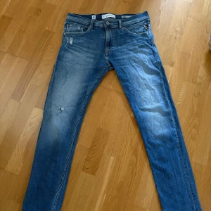 Tvär feta Replay jeans med slitningar - Säljer ett par blå Replay jeans i modellen Jondrill 05 aged. Jeansen har snygga slitningar och en tvättad look, klassisk femficksdesign och raka bakfickor med Replay-logga. Materialet är mjukt jeans i bomull med lite stretch för extra komfort. 