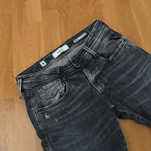 Replay Anbass aged 05 - Säljer ett par Replay Anbass jeans i svart tvättad denim med snyggt slitna detaljer. Modellen är skinny fit med klassiska fem fickor och diskret Replay-logga på bakfickan. Perfekta för dig som gillar en smal siluett och streetkänsla.