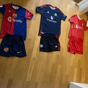 Manchester United mörkblå fotbollströja - Snygg Manchester United fotbollströja i mörkblått med röda detaljer och vita loggor. Tröjan har korta ärmar, rund hals och är tillverkad i lätt, ventilerande material. Tryck med Snapdragon på bröstet och Rashford 10 på ryggen. Finns från storlek 104 till 176. I set