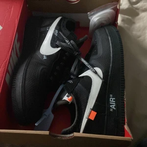 Nike Air Force 1 x Off-White svart/vit - Säljer ett par Nike Air Force 1 x Off-White i svart med vit swoosh och ikoniska Off-White-detaljer som texten 'AIR' på sulan och orange tag. Skorna har snörning, mesh och syntetmaterial samt coola kontrastdetaljer. Perfekta för dig som vill sticka ut.