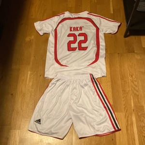 AC Milan Kaka 22 Champions League tröja - AC Milan bortaställ från Champions League-finalen 2007 med Kaka och nummer 22. Tröjan är vit med röda och svarta detaljer, broderat klubbmärke och guldtext om finalen. Setet är i polyester och har korta ärmar samt matchande shorts med klubbmärke och nummer.