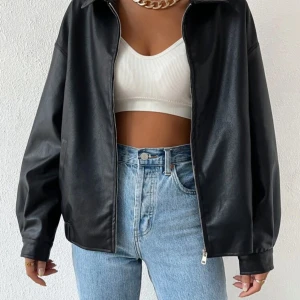 Svart skinnjacka med dragkedja - Snygg svart skinnjacka i modell med dragkedja framtill och klassisk krage. Jackan har raka ärmar och enkel design som passar till jeans eller kjol. Perfekt för dig som vill ha en stilren och edgy look.