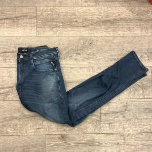 Replay Anbass blå jeans herr - Snygga Replay Anbass jeans i klassisk blå tvätt med lätt slitning. Modellen har fem fickor, smal passform och normal midja. Jeansen är tillverkade i stretchig denim för extra komfort och har Replay-logga på fickan. | Storlek: 33/32
