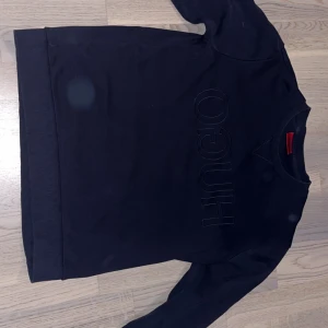 Svart sweatshirt från Hugo Boss - Mörkblå sweatshirt från Hugo Boss med diskret broderad HUGO-logga framtill. Tröjan har rund hals, långa ärmar och ribbade muddar vid ärmslut och nederkant. Tillverkad i mjuk bomull för en skön och avslappnad stil. Tröjan är en favorit men passar tyvärr inte längre den är i perfekt skick storlek S passar även Xs och M