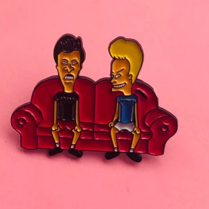 Beavis & Butt-Head pin - Cool emaljpin med Beavis & Butt-Head som sitter på en röd soffa. Färgglad design med svarta, röda, gula och blå detaljer. Perfekt att sätta på jackan eller väskan för en retro vibe. Hämtas i Hornstull i Stockholm eller skickas mot fraktkostnad. ❤️