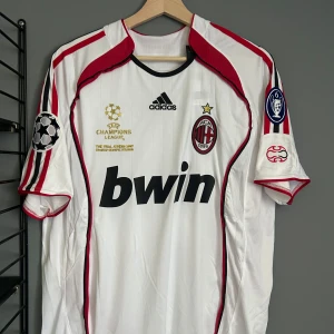 AC Milan Kaka Champions League tröja - Säljer en vit AC Milan fotbollströja från Adidas med Kaka och nummer 22 på ryggen. Tröjan har svarta och röda detaljer, Champions League-märken på ärmarna och Bwin som sponsor på bröstet. Klassisk passform med korta ärmar och broderat klubbmärke framtill. Helt ny med tagg en replika