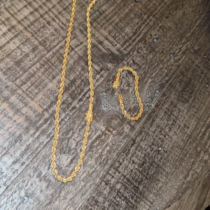 Guldfärgat halsband och armband set - Säljer ett snyggt set med guldfärgat halsband och matchande armband. Båda har en tvinnad kedjedesign som ger en cool och lyxig känsla. Perfekt för dig som vill sticka ut med accessoarer som verkligen syns.