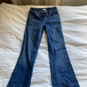 Blå bootcut jeans med broderade fickor - Snygga blå jeans med bootcut-modell och coola broderade detaljer på bakfickorna. Klassisk femficksdesign, normal midja och tillverkade i mjukt denimtyg. Perfekta för dig som gillar en retroinspirerad look med lite extra edge.