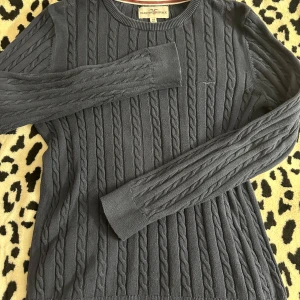 Mörkblå kabelstickad tröja Hampton Republic - Kabelstickad mörkblå tröja från Hampton Republic med rund halsringning och långa ärmar. Klassisk och stilren look med ribbade muddar och diskret broderad logga på bröstet. Perfekt för lager-på-lager under höst och vinter.