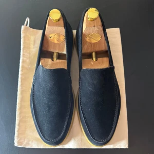 Loro Piana Summer Walk - Mörkblå loafers från Loro Piana i mjuk mocka med klassisk, stilren design och ljus gummisula. Perfekta för en clean och avslappnad look, med diskreta sömmar och bekväm passform. Modellen heter Summer Walk och är riktigt snygg till både jeans och chinos. Vet inte vad de gula fläckarna är på sulan, men det lär slitas bort medans man använder dem
