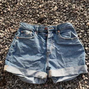Högmidjade jeansshorts med uppvik - Klassiska blå jeansshorts med hög midja och breda uppvikta benslut. Femficksmodell med knapp och dragkedja framtill, samt snygga kontrastsömmar. Perfekta för varma dagar och enkel att matcha med allt.