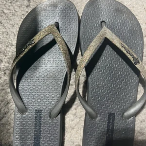 Havaianas  - Svarta flip-flop sandaler från Havaianas med glittriga remmar i guldton. Snyggt mönstrad sula och klassisk form, perfekta för sommardagar.