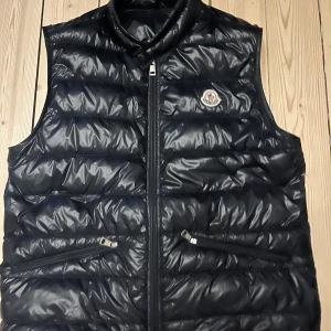 Svart Moncler GUI väst - Säljer min moncler GUI väst som är i väldigt fin skick, säljer pga har ej användning. Skick 9/10, knappt använd, storlek 3/M