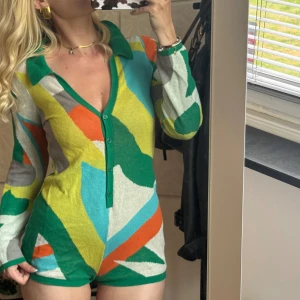 Färgglad stickad jumpsuit  - Superunik stickad jumpsuit från Jaded London. Djup v-ringning, krage och knappar framtill. Långärmad och figurnära passform, perfekt för dig som vill sticka ut.