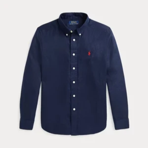 Ralph lauren skjorta  -  Strlk S-M Klassisk mörkblå skjorta från Polo Ralph Lauren i 100% bomull. Skjortan har långa ärmar, knappar framtill och ikonisk röd broderad logga på bröstet. Perfekt för dig som gillar stilrena och tidlösa plagg med snygga detaljer.