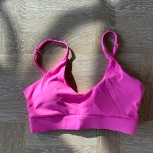 Rosa linnetopp med smala axelband - Snygg rosa linnetopp med smala, justerbara axelband och bred resår under bysten. Perfekt för en färgstark look och superbekväm att bära. Enkel design som ger en sportig vibe.