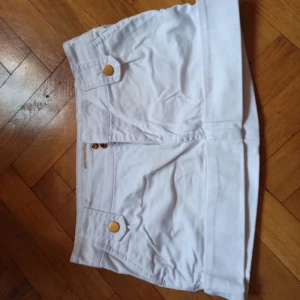 Vit minikjol  - Vit kort jeanskjol från Calliope Denim med snygga guldknappar och dragkedja framtill. 