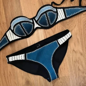 Blå och vit bikini från Triangl - Snygg bikini från Triangl i blått och vitt med coola kontrastsömmar och broderade detaljer. Överdelen har bygel och vadderade kupor, underdelen har matchande broderier. Både topp och trosa har svarta kanter som ger en edgy look. Perfekt för stranden eller poolen!