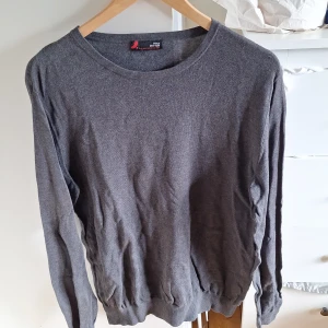 Mörkgrå tröja från Dressmann - En stilren mörkgrå tröja från Dressmann i mjuk pima bomull, perfekt tunn nu för sommaren. Tröjan har rund halsringning, långa ärmar och ribbade muddar vid ärmslut och nederkant. Perfekt för dig som gillar en enkel och klassisk look. Tyvärr saknas lapp för storlek men skulle säga att det är en L!