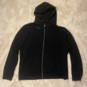 Svart zipteöja från lager 157 - En klassisk svart zipteöja från lager 157. Tröjan har hel dragkedja framtill, huva med snörning och långa ärmar. Perfekt för chill dagar eller när du vill ha en enkel och stilren look.