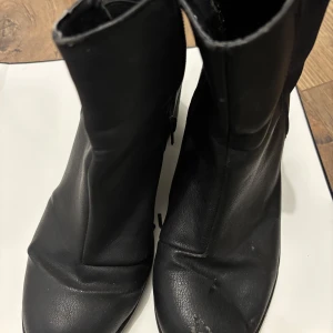Svarta boots från Impuls i skinn - Svarta boots från Impuls i äkta skinn med rund tå och dragkedja på insidan. Klassisk och stilren modell som passar till det mesta. Bootsens ovandel är slät och de har en platt sula för bekväm känsla hela dagen.
