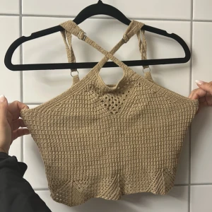 Beige stickad croppad linnetopp - Säljer en beige stickad linnetopp med snygga korsade axelband och virkad detalj framtill. Toppen är croppad och har justerbara band för perfekt passform. Perfekt för varma dagar och ger en chill boho-vibe.