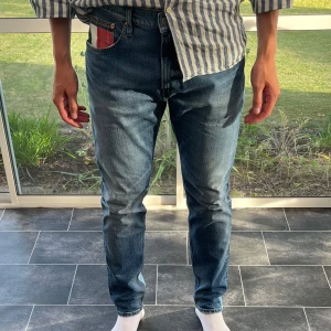 Tommy Jeans blå jeans W32/L34 - Säljer ett par klassiska blå jeans från Tommy Jeans i storlek 32/34. Jeansen har normal passform, raka ben och snygga detaljer som det ikoniska Tommy-fodrade myntfacket och logga på bakfickan. Tillverkade i slitstarkt bomullsjeans med snygg tvätt.