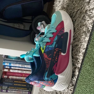 Färgglada sneakers från Puma - Säljer ett par riktigt färgstarka sneakers från Puma med turkosa snören, rosa och blå detaljer samt coola grafiska mönster på sidorna. Ovandelen är i mesh och mocka, med vit sula och rund tå. Perfekta för dig som vill sticka ut med din stil.