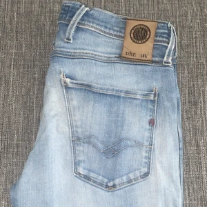 Replay Anbass ljusblå jeans - Snygga Replay Anbass jeans i ljusblå färg med slitningar och en liten reva på ena benet. Klassisk femficksmodell med Replay-logga på fickan och läderpatch bak. Jeansen har en modern passform och är perfekta för en avslappnad stil. Pris kan absolut diskuteras!