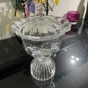 Glasskål -  en dekorativ glasskål med lock och fot, . Skålen har ett elegant, räfflat mönster och passar perfekt för godis, snacks . Vintage vet ej vilket år . Perfekt för att ge din inredning en vintagekänsla eller som en snygg detalj på skrivbordet.kan möta er i Stockholm city