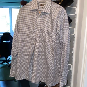 Rutig skjorta från Ströms, stl 44 - Klassisk rutig skjorta från Ströms i regular fit. Skjortan är vit med blå och bruna rutor, har lång ärm, bröstficka och knäppning framtill. Perfekt för dig som gillar en stilren och tidlös look.