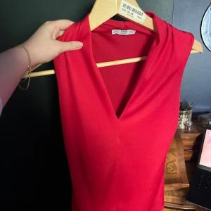 Röd ärmlös body med v-ringning Zara - Snygg röd ärmlös body från Zara med djup v-ringning och mjukt, stretchigt material. Perfekt för dig som vill ha en enkel men ändå iögonfallande look. Passar till både jeans och kjol för en trendig vibe.