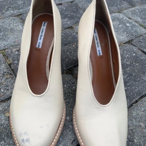 Beige pumps från & other stories i skinn - Snygga pumps i beige skinn med rund tå och kraftig hög klack. Skorna har en stilren design med markerad sula och ljusa sömmar runt kanten. Perfekta för dig som gillar minimalistisk och modern stil. Finns en liten fläck som kan poleras bort