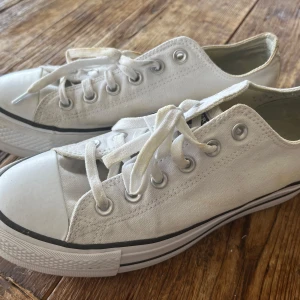 Vita Converse All Star sneakers - Klassiska vita Converse All Star sneakers i canvas med lågt skaft. Skorna har vita snören, silverfärgade öljetter och en vit gummisula med svart rand. Perfekta för en avslappnad och cool stil. Rund tå och platt sula för skön känsla hela dagen.