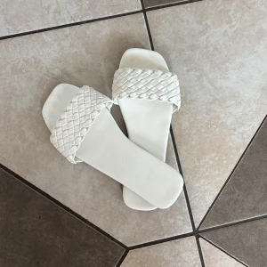 Vita flätade sandaler. - Snygga vita sandaler med bred, flätad rem över foten och fyrkantig tå. Platt sula och stilren design som passar perfekt till sommarens outfits. Tillverkade i syntetmaterial för en fräsch look. Storlek 36