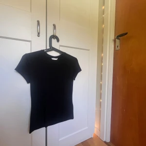 Svart kortärmad topp från H&M - En svart, enkel och tight topp från H&M i storlek S. Modellen är klassisk med rund halsringning och korta ärmar. Perfekt att styla med jeans eller kjol för en clean look. Materialet är mjukt och stretchigt för en bekväm passform, använt fåtal gånger 💖