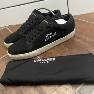 Saint Laurent skor - Svarta sneakers från Saint Laurent med vit sula och broderad logga på sidan. Skorna har snörning, rund tå och är tillverkade i canvas och skinn. Klassisk och stilren design med diskreta detaljer och Saint Laurent Paris-tryck på plösen och sulan. Och en dustbag ingår och vid en snabb afär går de att diskutera priset