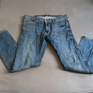 Blå Lee jeans straight fit - Klassiska blå jeans från Lee med rak passform och normal midja. Jeansen har fem fickor, Lee-lapp bak i brunt läder och snygga slitningar för en avslappnad look. Perfekta till sneakers eller boots och funkar året runt. Hör gärna av er vid minsta lilla fråga 