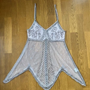 Glittrig linne-topp från Saint Tropez - Supersnygg glittrig linne-topp från Saint Tropez i ljusrosa mesh med silverpaljetter och pärlbroderier. Toppens spetsiga nederkant och tunna axelband ger en unik look. Perfekt för dig som vill sticka ut med en transparent och festlig vibe.