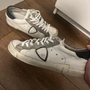 Philippe Model  - Säljer ett par Philippe Model sneakers i vitt och grått med svarta detaljer. Skorna har snörning, de är i storlek 42. Några få defekter som syns på bild. T.ex vid hälen.