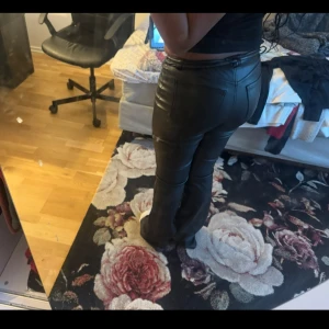 Svarta skinnbyxor med bootcut - Säljer ett par svarta skinnbyxor med bootcut passform. Byxorna har hög midja och klassiska bakfickor. Snyggt glansigt material som ger en edgy vibe och passar perfekt till en trendig outfit.