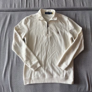 Beige Polo Ralph Lauren quarterzip - Säljer en helt oanvänd Polo Ralph Lauren quarterzip färgad beige. Tröjan är i storlek M och är i extremt bra skick och eftersom den är helt oanvänd. Originalpriset på denna ligger på 2500kr
