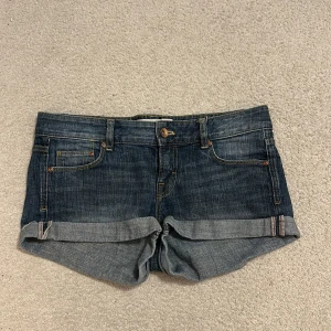 Mörkblå jeansshorts med upprullad kant - Snygga mörkblå jeansshorts från HM med klassisk femficksdesign och upprullad kant. Shortsen har låpgmidjad passform, bälteshällor och detaljerade sömmar. Perfekta för varma dagar när du vill ha en avslappnad och cool stil.