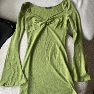 Grön långärmad klänning från SHEIN - Snygg grön klänning från SHEIN med lång ärm och twistad detalj vid bysten. Klänningen har en smickrande v-ringning och lätt utsvängda ärmar. Perfekt för dig som gillar en enkel men trendig look.