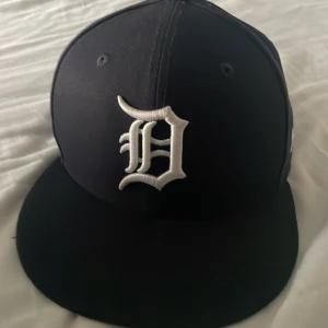 Svart New Era Detroit Tigers keps - Snygg svart keps från New Era med Detroit Tigers-logga broderad i vitt framtill. Klassisk flat brim och MLB-logga baktill. Kepsen har även New Era-loggan på sidan. Perfekt för dig som gillar sportig streetstyle.