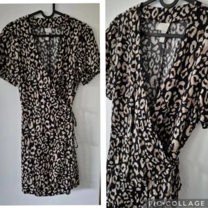 Leopardmönstrad omlottklänning - Snygg kort omlottklänning med leopardmönster i svart, beige och vitt. Klänningen har korta ärmar, knyt i midjan och v-ringad hals. Perfekt för dig som vill sticka ut med ett trendigt djurmönster.